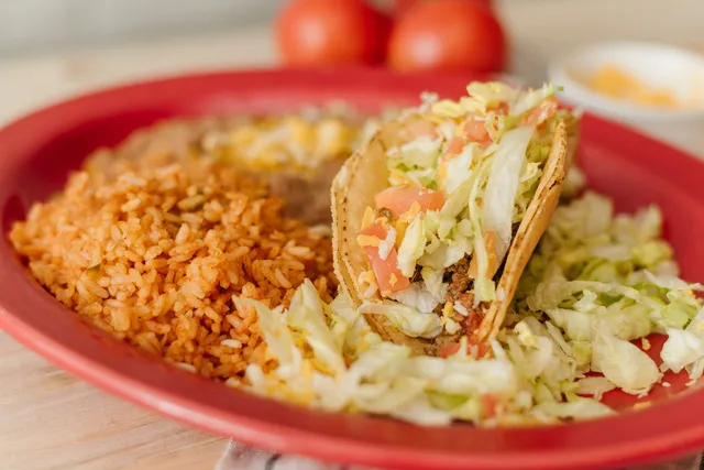 Crispy beef taco with lettuce, tomato, and cheese next to Mexican rice and refried beans, the same sides that come with a Su Casa taco bar