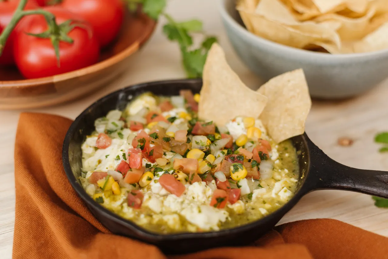 Queso dip with diced tomatoes and roasted corn in a cast-iron skillet, served with tortilla chips at Su Casa in Midvale